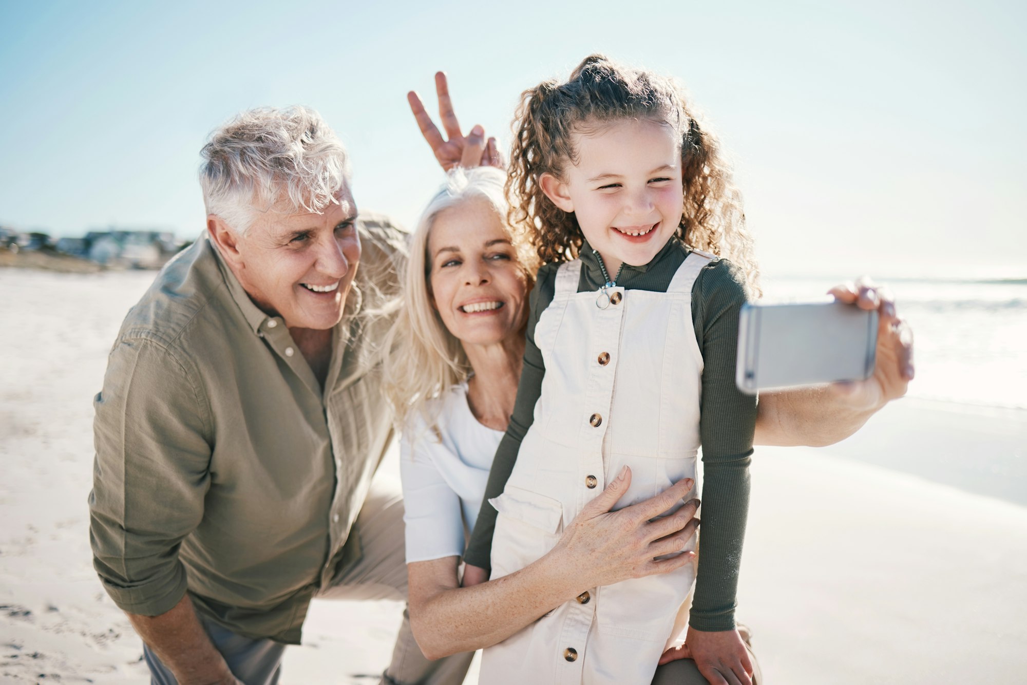 Family, selfie and beach holiday with peace sign, grandparents and young girl with a smile. Happy,